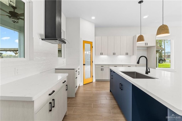 kitchen featuring wood tiled floor, a sink, hanging light fixtures, wall chimney range hood, and tasteful backsplash