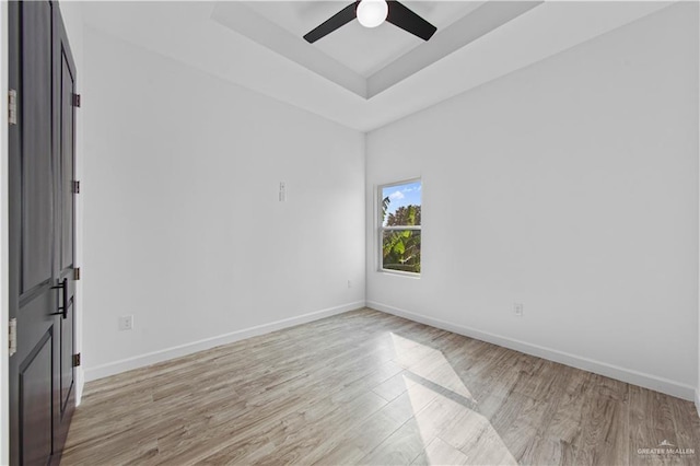 empty room featuring ceiling fan, a tray ceiling, and light hardwood / wood-style floors