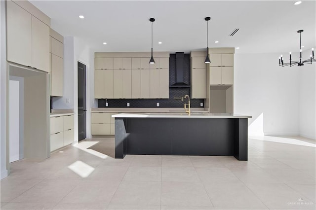 kitchen with decorative light fixtures, sink, backsplash, a kitchen island with sink, and wall chimney exhaust hood