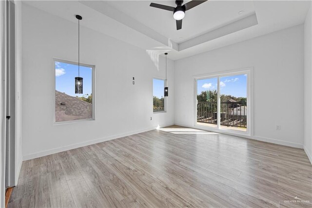 unfurnished living room with ceiling fan, a tray ceiling, light hardwood / wood-style floors, and a high ceiling