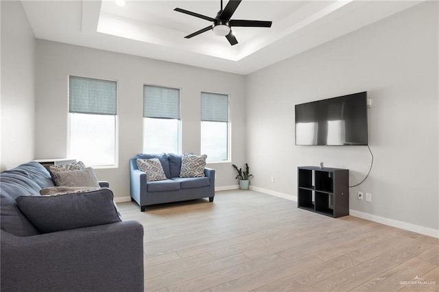 living room with ceiling fan, a raised ceiling, and light hardwood / wood-style flooring