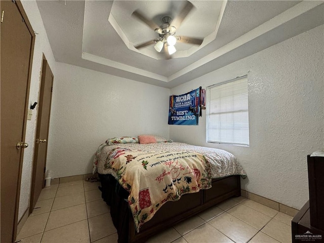 bedroom featuring ceiling fan, a raised ceiling, and light tile patterned floors