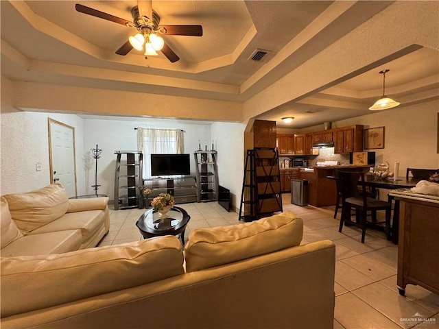 living room with a raised ceiling, ceiling fan, and light tile patterned floors