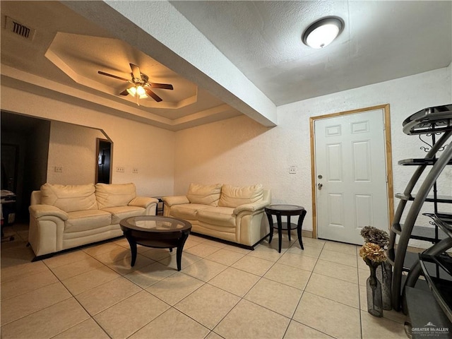 tiled living room with a tray ceiling, ceiling fan, and a textured ceiling