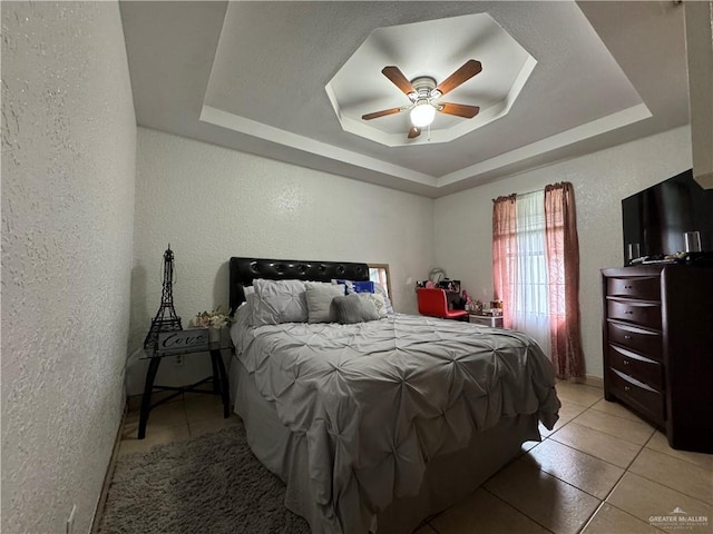 tiled bedroom with a raised ceiling and ceiling fan