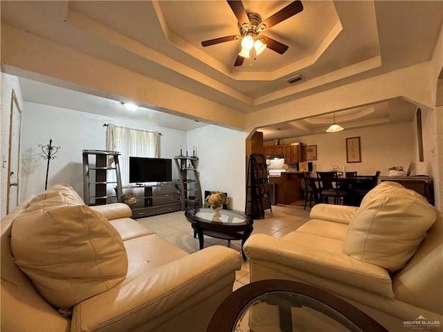 tiled living room with ceiling fan and a tray ceiling