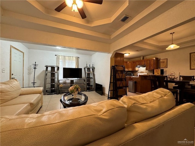 tiled living room with ceiling fan and a tray ceiling