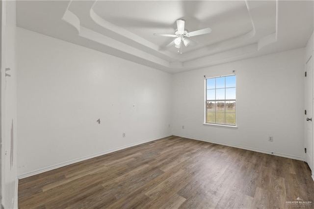 unfurnished room with ceiling fan, dark hardwood / wood-style flooring, and a tray ceiling