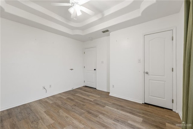 unfurnished bedroom with ceiling fan, wood-type flooring, and a tray ceiling