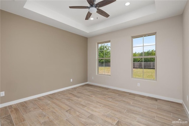 spare room with a raised ceiling, ceiling fan, and light hardwood / wood-style flooring