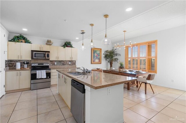 kitchen with stainless steel appliances, sink, cream cabinets, hanging light fixtures, and an island with sink