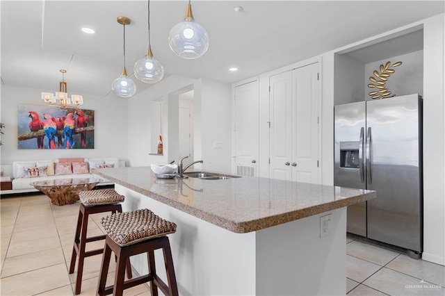 kitchen with a kitchen bar, stainless steel refrigerator with ice dispenser, sink, pendant lighting, and light tile patterned flooring