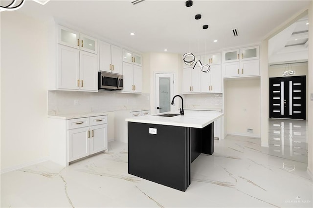 2809 E Tamarindo Ave, Hidalgo, TX 78557 - kitchen featuring stainless steel microwave, light marble finish floors, a kitchen island with sink, backsplash, and glass insert cabinets