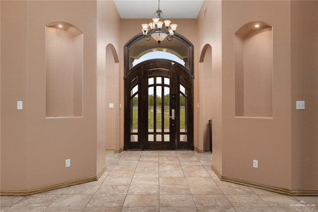 tiled entrance foyer with baseboards, a notable chandelier, and arched walkways