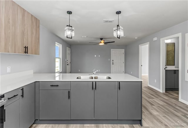 kitchen featuring kitchen peninsula, gray cabinets, hanging light fixtures, and light hardwood / wood-style floors