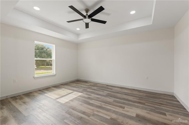 unfurnished room featuring a tray ceiling, ceiling fan, and hardwood / wood-style flooring