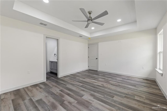 unfurnished room featuring a wealth of natural light, a tray ceiling, dark hardwood / wood-style floors, and ceiling fan