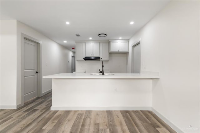 kitchen with kitchen peninsula, sink, white cabinets, and light hardwood / wood-style floors