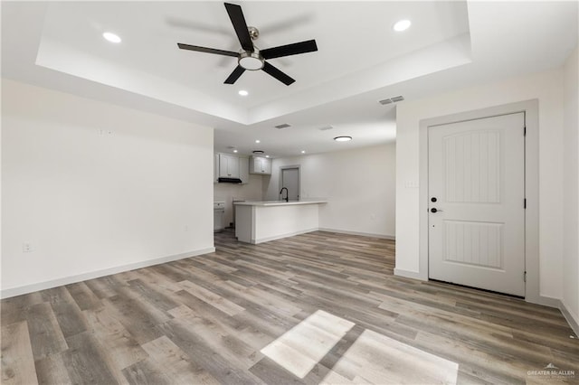 unfurnished living room with light hardwood / wood-style floors, a raised ceiling, ceiling fan, and sink