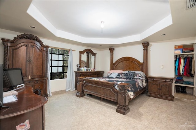 bedroom with a tray ceiling, a walk in closet, a closet, and ornate columns