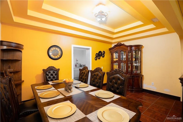 dining area with dark tile patterned flooring and a raised ceiling