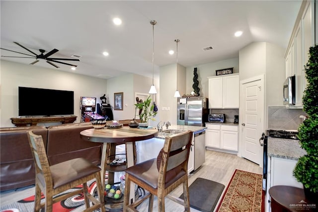 kitchen with ceiling fan, stainless steel appliances, pendant lighting, decorative backsplash, and light wood-type flooring