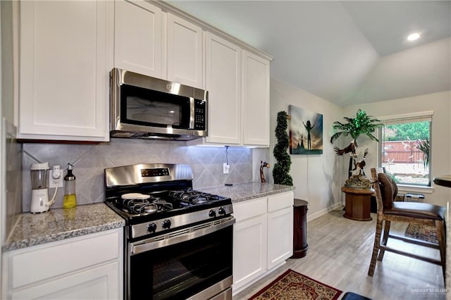 kitchen with light stone countertops, white cabinetry, appliances with stainless steel finishes, and vaulted ceiling