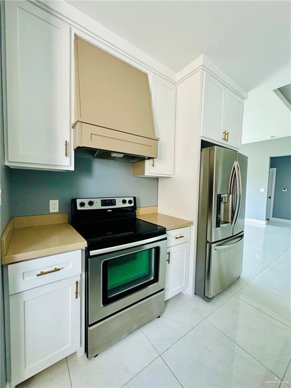 2802 Garman St, Edinburg, TX 78542 - kitchen featuring stainless steel appliances, custom exhaust hood, white cabinetry, light countertops, and light tile patterned flooring