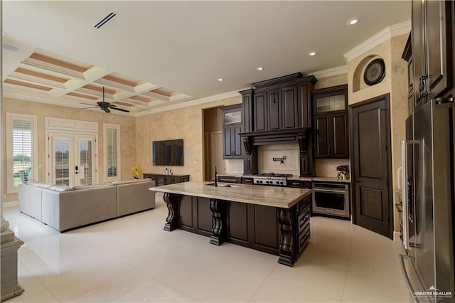 kitchen featuring a kitchen breakfast bar, coffered ceiling, stainless steel appliances, an island with sink, and dark brown cabinetry