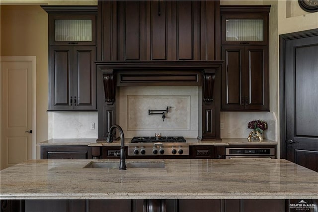 kitchen featuring light stone countertops, stainless steel appliances, an island with sink, dark brown cabinetry, and sink