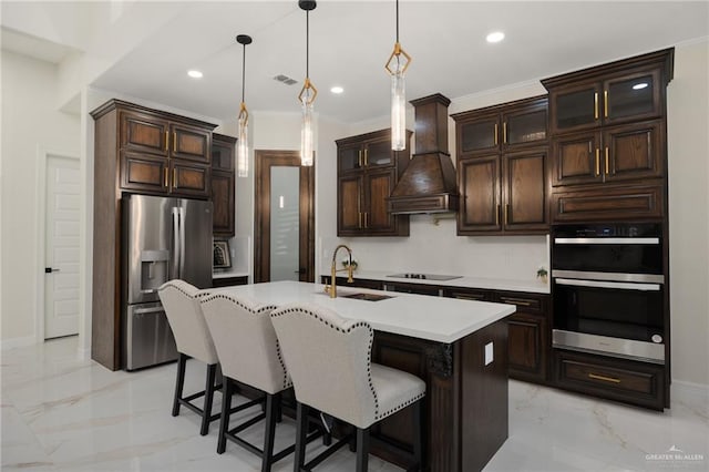 kitchen with custom exhaust hood, sink, an island with sink, decorative light fixtures, and stainless steel appliances