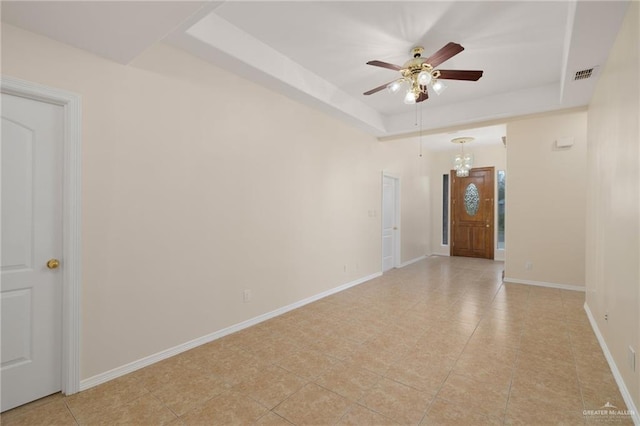 tiled empty room featuring ceiling fan with notable chandelier and a tray ceiling