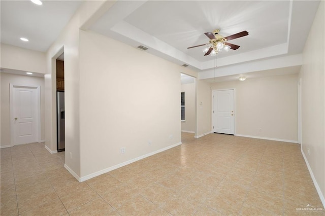 spare room featuring a raised ceiling, ceiling fan, and light tile patterned flooring