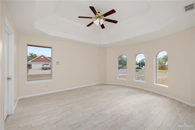 spare room featuring a tray ceiling, ceiling fan, and light hardwood / wood-style flooring