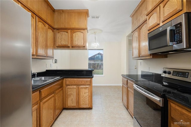 kitchen with sink, dark stone countertops, light tile patterned floors, appliances with stainless steel finishes, and a notable chandelier