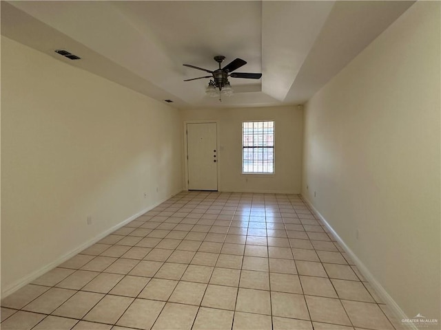 empty room with light tile patterned floors, visible vents, a raised ceiling, baseboards, and ceiling fan