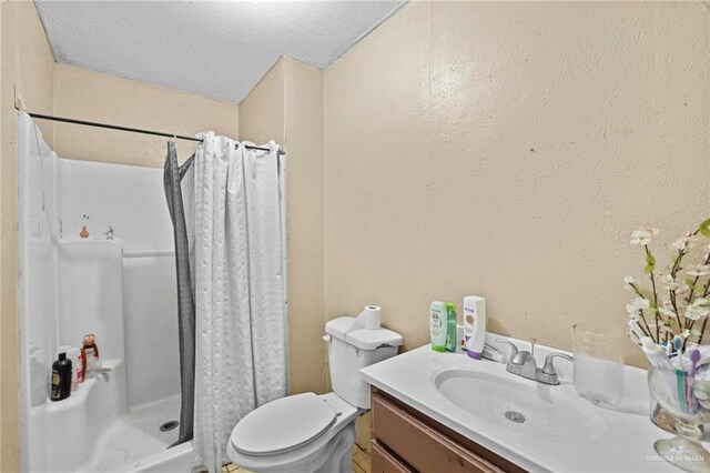 bathroom with a textured ceiling, vanity, toilet, and walk in shower