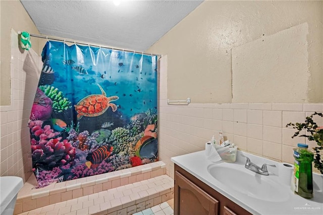 bathroom featuring vanity, a textured ceiling, toilet, and tile walls