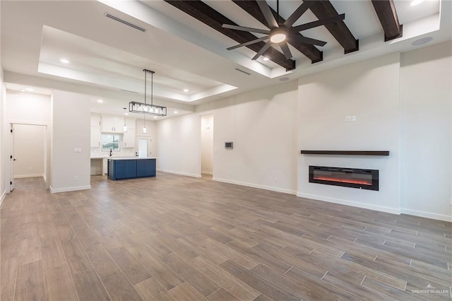 unfurnished living room featuring ceiling fan, a tray ceiling, and sink