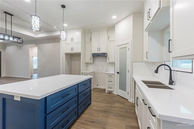 kitchen featuring blue cabinetry, sink, white cabinetry, a center island, and hanging light fixtures