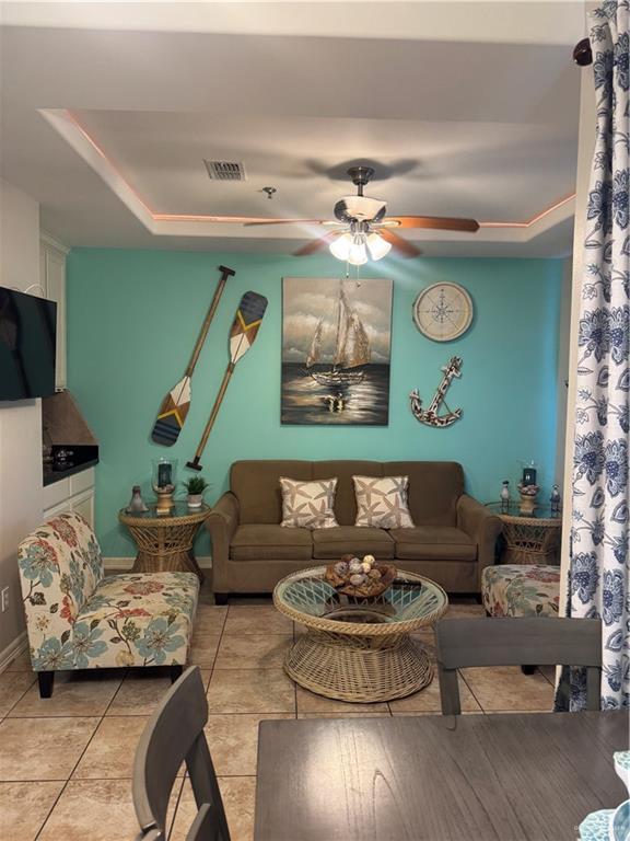 living area with visible vents, a tray ceiling, a ceiling fan, and light tile patterned flooring