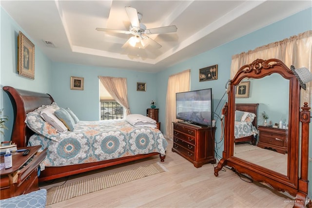 bedroom featuring ceiling fan, a raised ceiling, and light hardwood / wood-style flooring