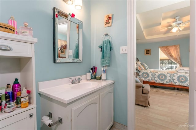 bathroom featuring hardwood / wood-style floors, vanity, a tray ceiling, and ceiling fan