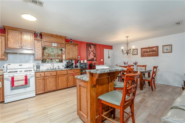 kitchen with a center island, an inviting chandelier, decorative light fixtures, a kitchen bar, and white gas range oven