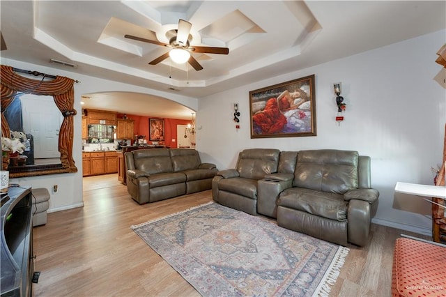 living room featuring ceiling fan with notable chandelier, light wood-type flooring, a raised ceiling, and sink