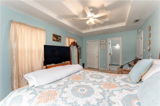 bedroom featuring ceiling fan, ensuite bathroom, and a tray ceiling