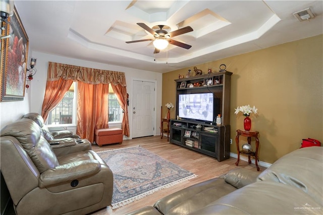 living room featuring light hardwood / wood-style floors, a raised ceiling, and ceiling fan