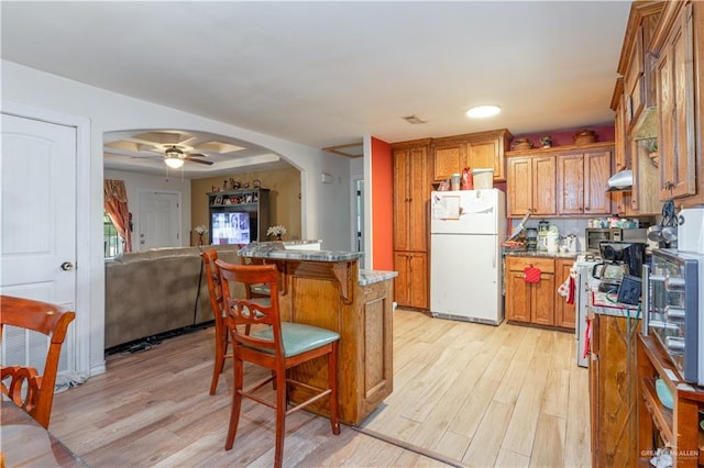 kitchen featuring white fridge, light hardwood / wood-style flooring, ceiling fan, and a tray ceiling