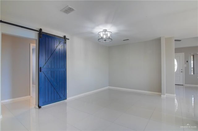 empty room with a chandelier, visible vents, baseboards, and a barn door