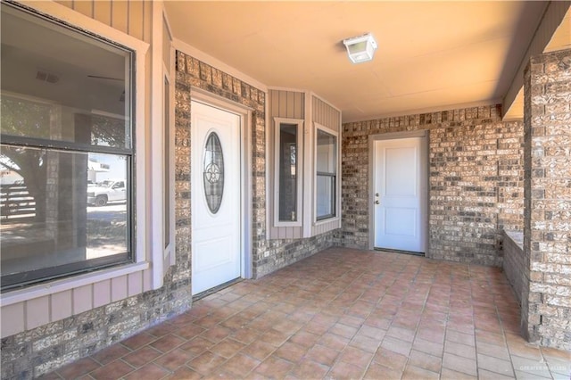 view of exterior entry featuring visible vents, board and batten siding, and brick siding